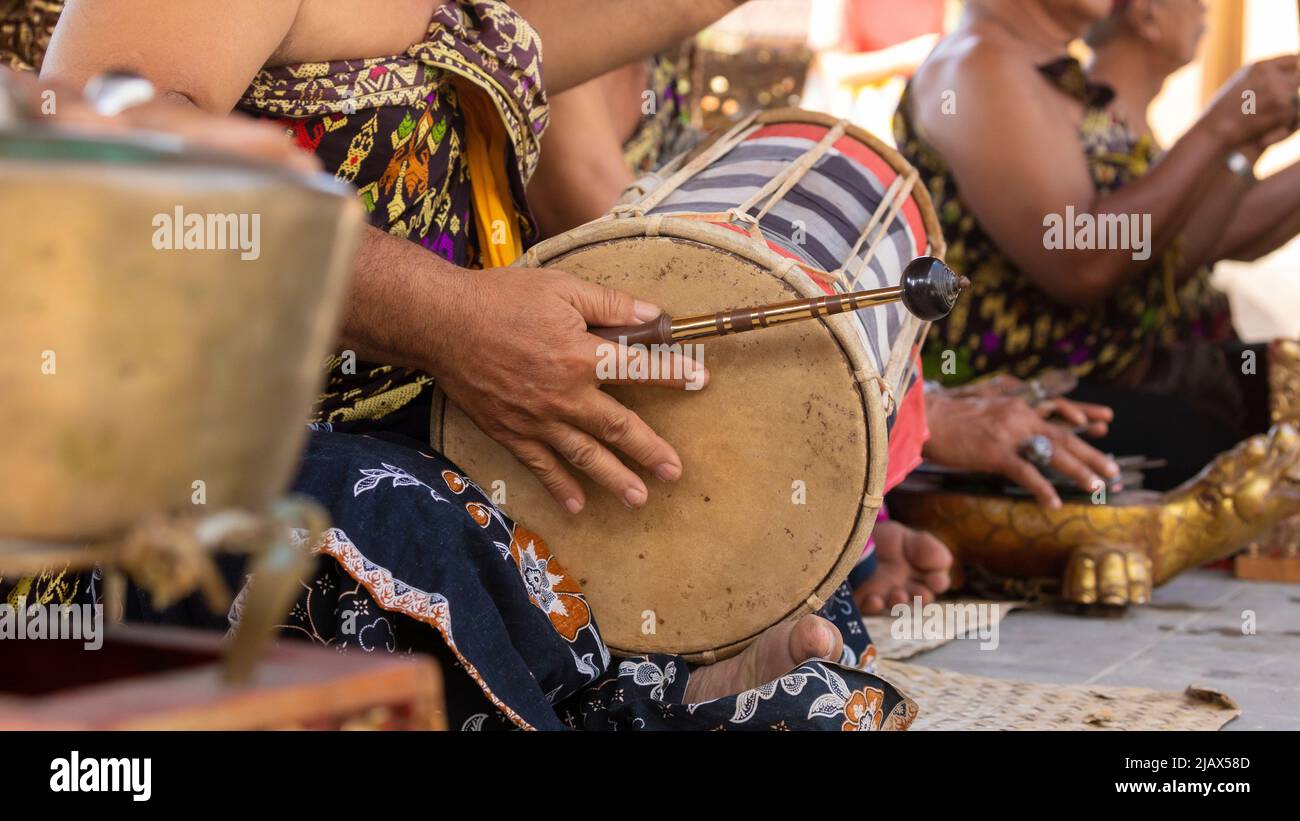 A musician plays a kendhang or ketipung, a traditional Balinese instrument, as part of a musical ensemble or gamelan, during a performance Stock Photo