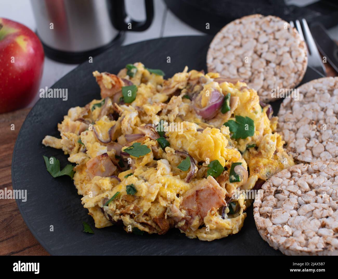 Workout meal with scrambled eggs, ham, onions and herbs. Served with brown rice cracker on a plate Stock Photo
