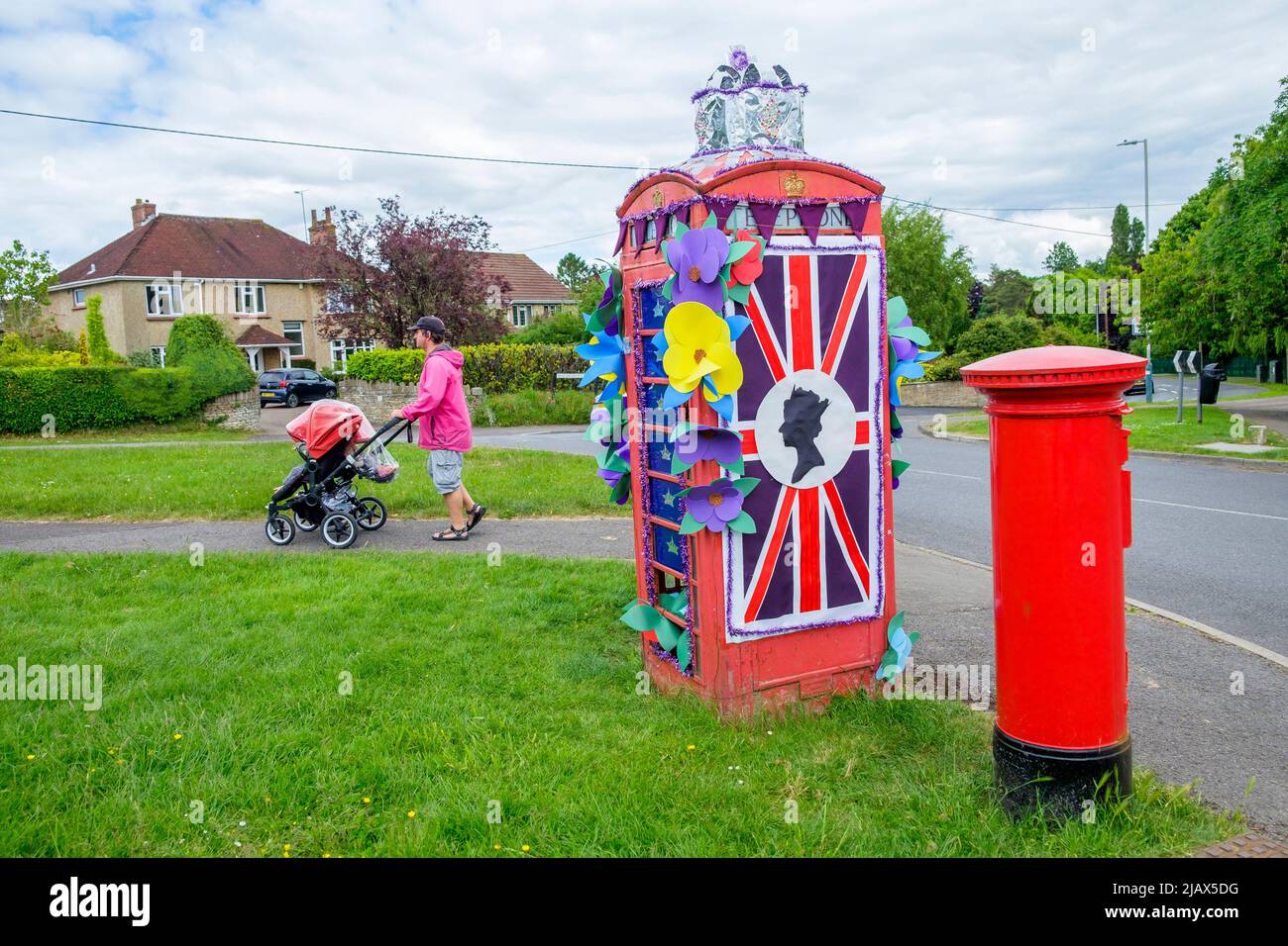 Chippenham, Wiltshire, UK. 1st June, 2022. A day before the long bank holiday weekend starts, a man pushing a child in a buggy is pictured as he walks past a phone box that has been decorated to celebrate the Queen's Platinum Jubilee.  Credit: Lynchpics/Alamy Live News Stock Photo