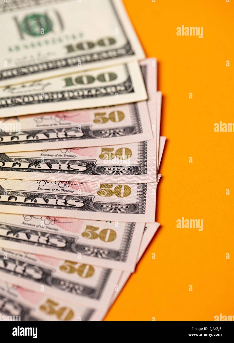 Spread out fifty dollar banknotes, one hundred dollar bills on top. Orange background behind USD currency Stock Photo