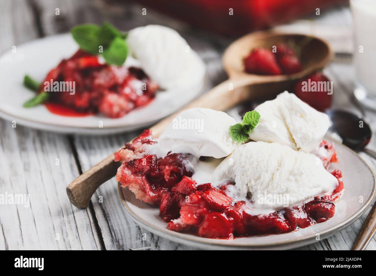 Sweet homemade strawberry cobbler or Sonker with French vanilla ice cream over a rustic white wood table. Extreme selective focus with blurred backgro Stock Photo