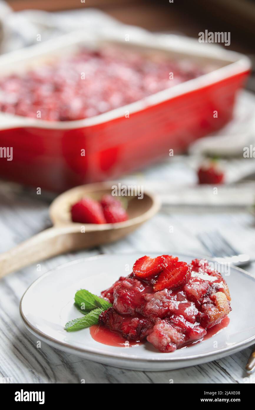 Sweet homemade strawberry cobbler or Sonker baked in a red ceramic pan over a rustic white wood table. Extreme selective focus with blurred background Stock Photo