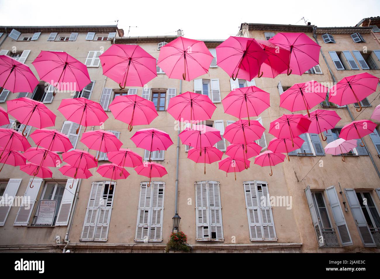 Historic Center of Grasse, France on September 9, 2021. The historic center of Grasse was once home to perfume factories that have since moved out of the old town. Pink umbrellas are suspended above the streets every May through October, representing the Grasse May rose - an ingredient in the iconic Chanel No. 5. - which blooms only in May. Grasse has had a prospering perfume industry since the end of the 18th century and is considered the world's capital of perfume. There are numerous of old 'parfumeries' in Grasse, such as Galimard, Molinard and Fragonard, each with tours and a museum. Many Stock Photo