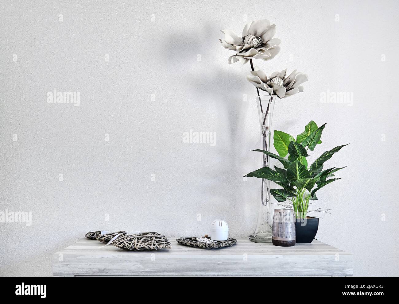 Potted green natural and grey artificial flowers in vase with cute home accessories on table over white wall background, copy space Interior Stock Photo