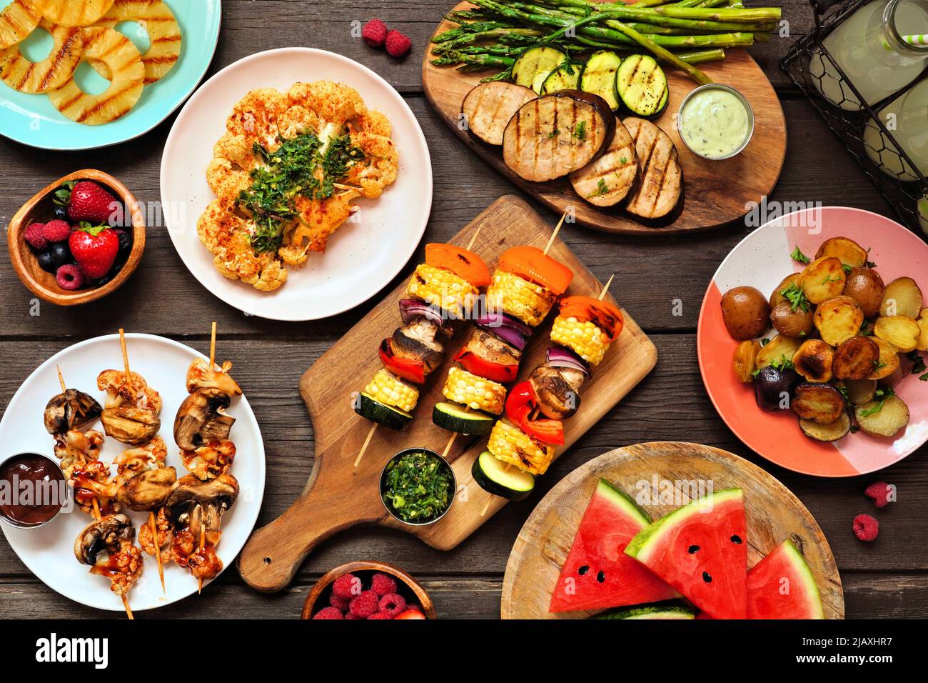 Healthy plant based summer bbq table scene. Top view on a dark wood background. Grilled fruit and vegetables, skewers, cauliflower steak and vegetaria Stock Photo