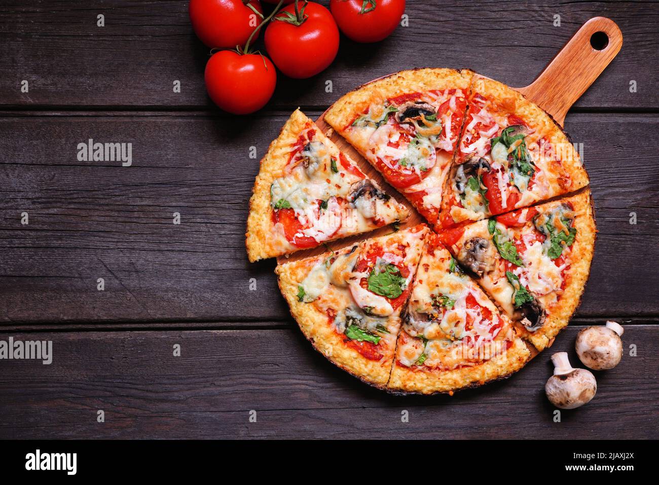 Healthy, gluten free cauliflower crust pizza with tomatoes, mushrooms and spinach. Top down view with cut slices. Table scene on a dark wood backgroun Stock Photo