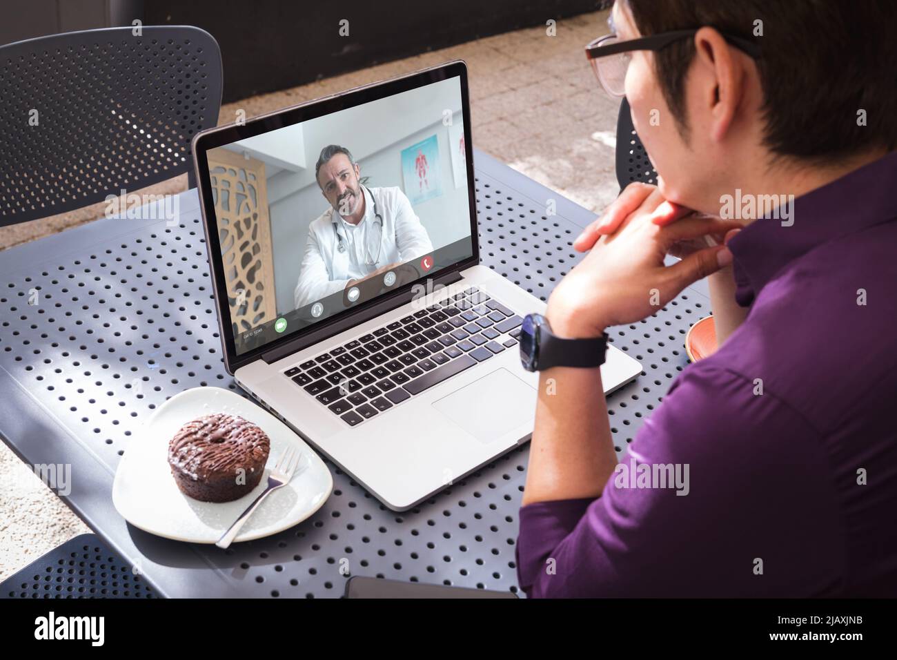 Asian young man sitting with hand on chin while talking to caucasian mature male doctor on laptop Stock Photo