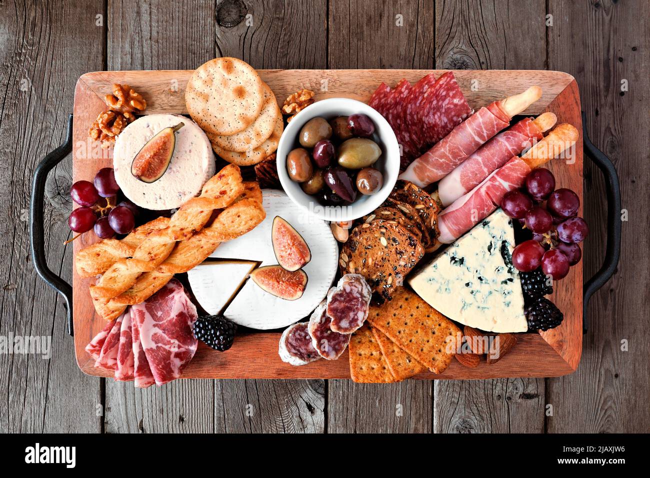 Charcuterie tray of a variety of meats, cheeses and appetizers. Top view on a dark wood background. Stock Photo