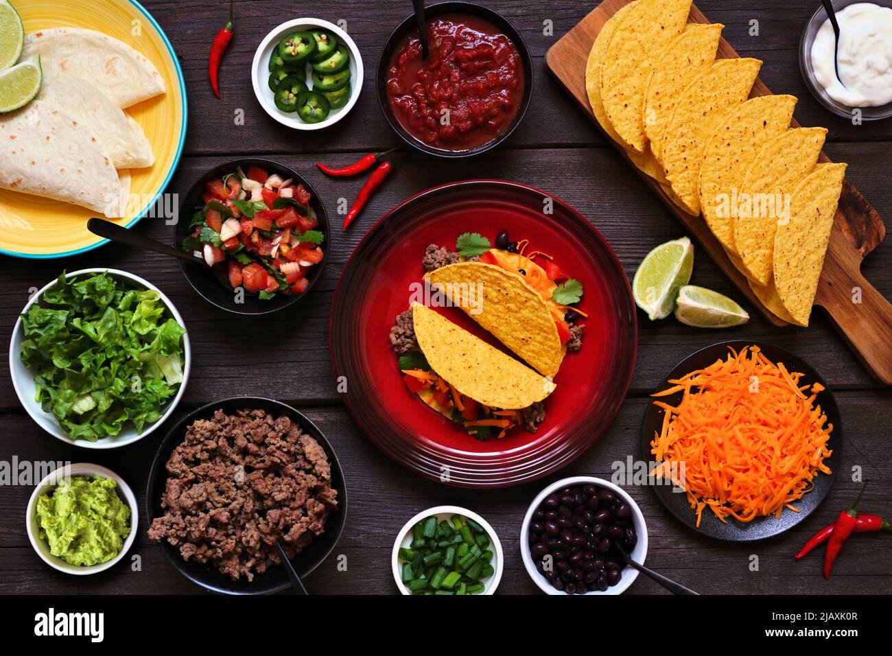 Taco bar table scene with a selection of ingredients. Above view on a dark wood banner background. Mexican food buffet. Stock Photo