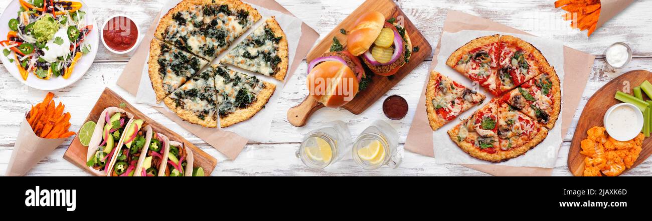 Healthy plant based fast food table scene. Overhead view on a white wood banner background. Cauliflower crust pizzas, bean burgers, mushroom tacos and Stock Photo