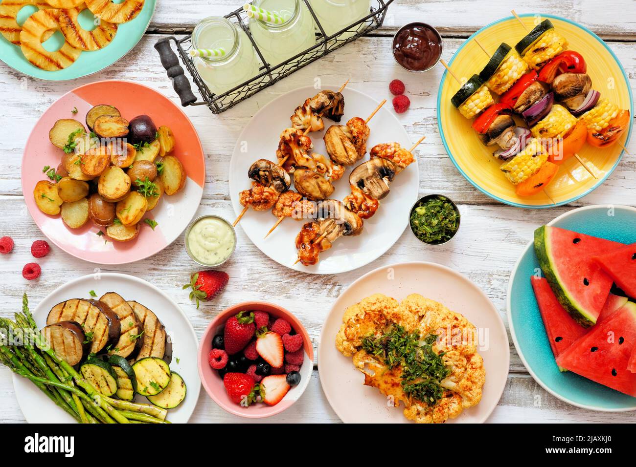 Vegan summer bbq or picnic table scene. Overhead view on a white wood background. Fruit, grilled vegetables, skewers, cauliflower steak and lemonade. Stock Photo