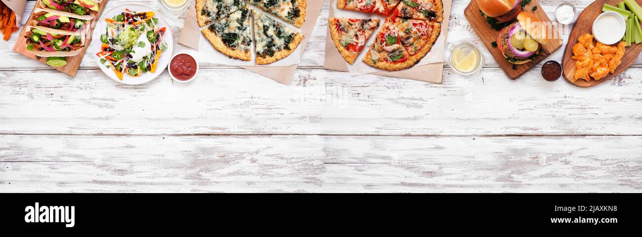 Healthy plant based fast food top border. Above view over a white wood banner background. Table scene with cauliflower crust pizzas, bean burgers, mus Stock Photo