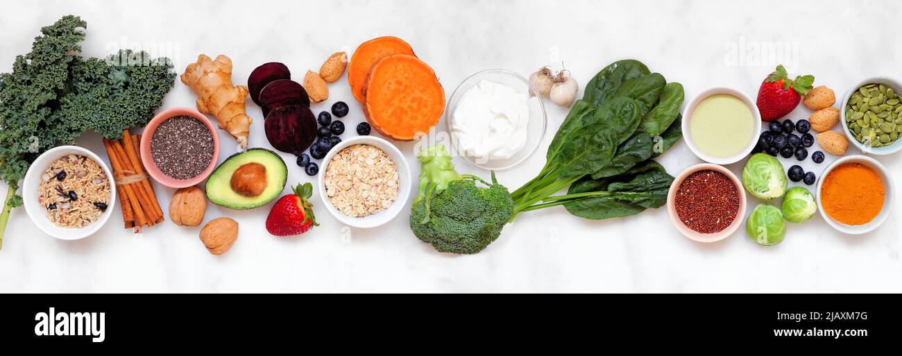 Set of healthy food ingredients. Top view table scene on a white marble banner background. Super food concept with green vegetables, berries, whole gr Stock Photo