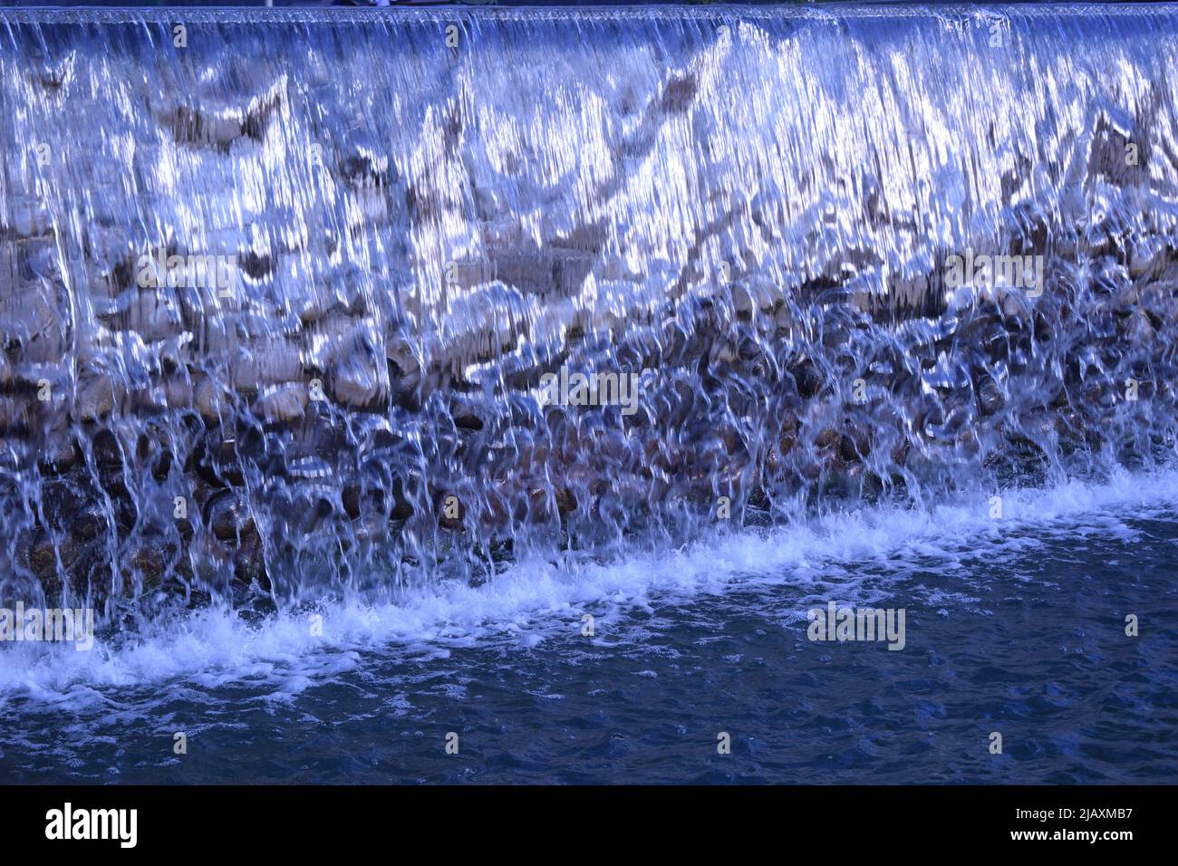 A waterfall flowing at park. A waterfall of a fountain in a garden. Wall of water. A beautiful view of the falling water cascade. Artificial waterfall Stock Photo