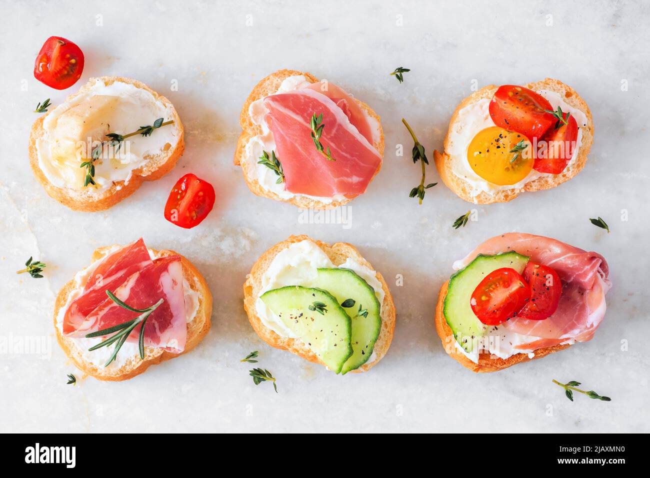 Assortment of cream cheese crostini hors d'oeuvres with a variety of toppings. Above view on a white marble background. Party food concept. Stock Photo