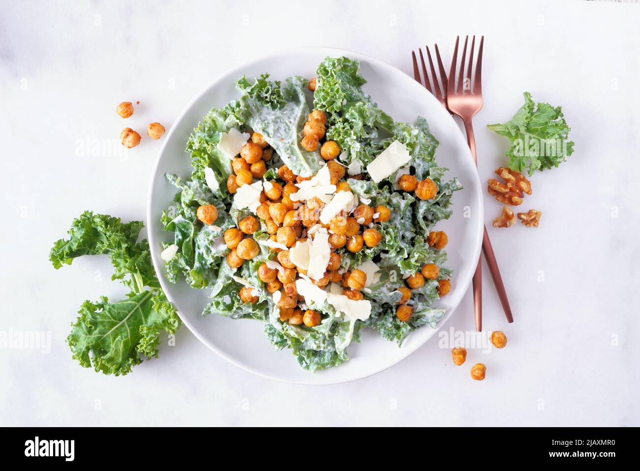 Vegetarian Caesar salad with chickpeas, kale and a yogurt dressing. Top view over a white marble background. Plant based food concept. Stock Photo