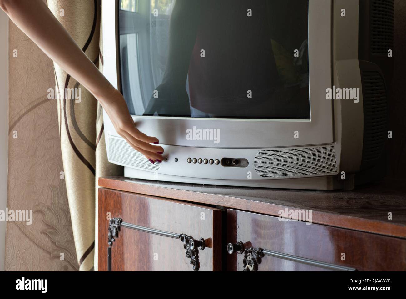 A woman's hand turns on an old gray TV in an apartment at home Stock Photo