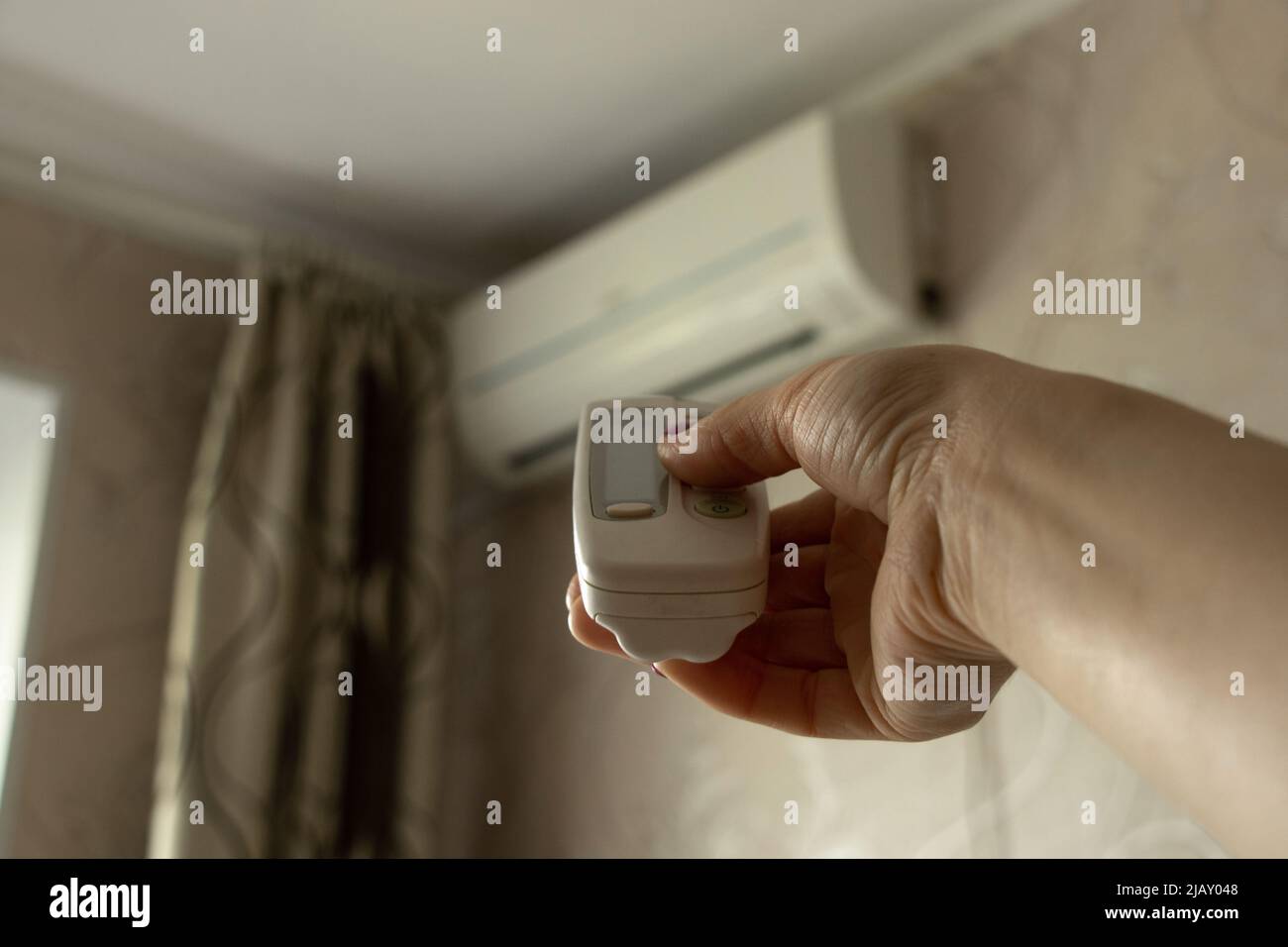 The remote control from the air conditioner in the girl's hand is directed to the air conditioner in the apartment, turn on the air conditioner, clima Stock Photo