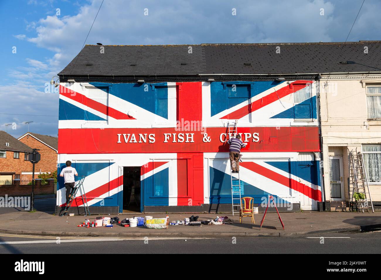 Cradley Heath, West Midlands, UK. 1st June, 2022. Chip shop proprietor Warren Rudge puts the finishing touches onto the Union Jackflag he and his son James have painted on their fish and chip shop in Cradley Heath, West Midlands. The painted flag covers the whole of Ivan's Fish and Chips frontage including the windows, and has taken all day to complete. 'Ivan's Fish and Chips has been serving fish and chips for 65 years - not quite as long as Her Majesty though. But I have heard that The Queen is partial to fish and chips.' says Warren. Credit: Peter Lopeman/Alamy Live News Stock Photo