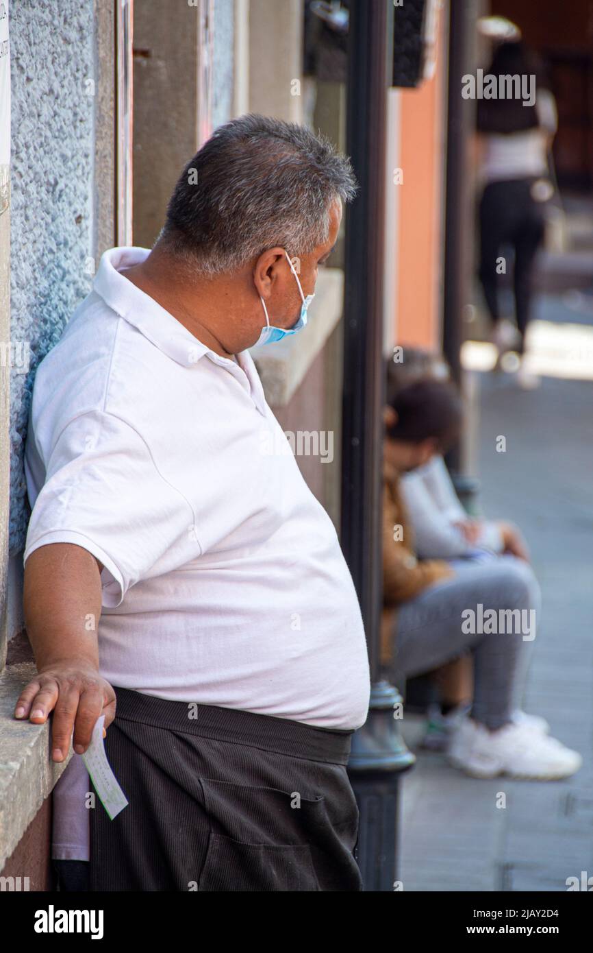 An overweight man wearing a mask, leaning against a wall. Guanajuato, Guanajuato, Mexico. Stock Photo