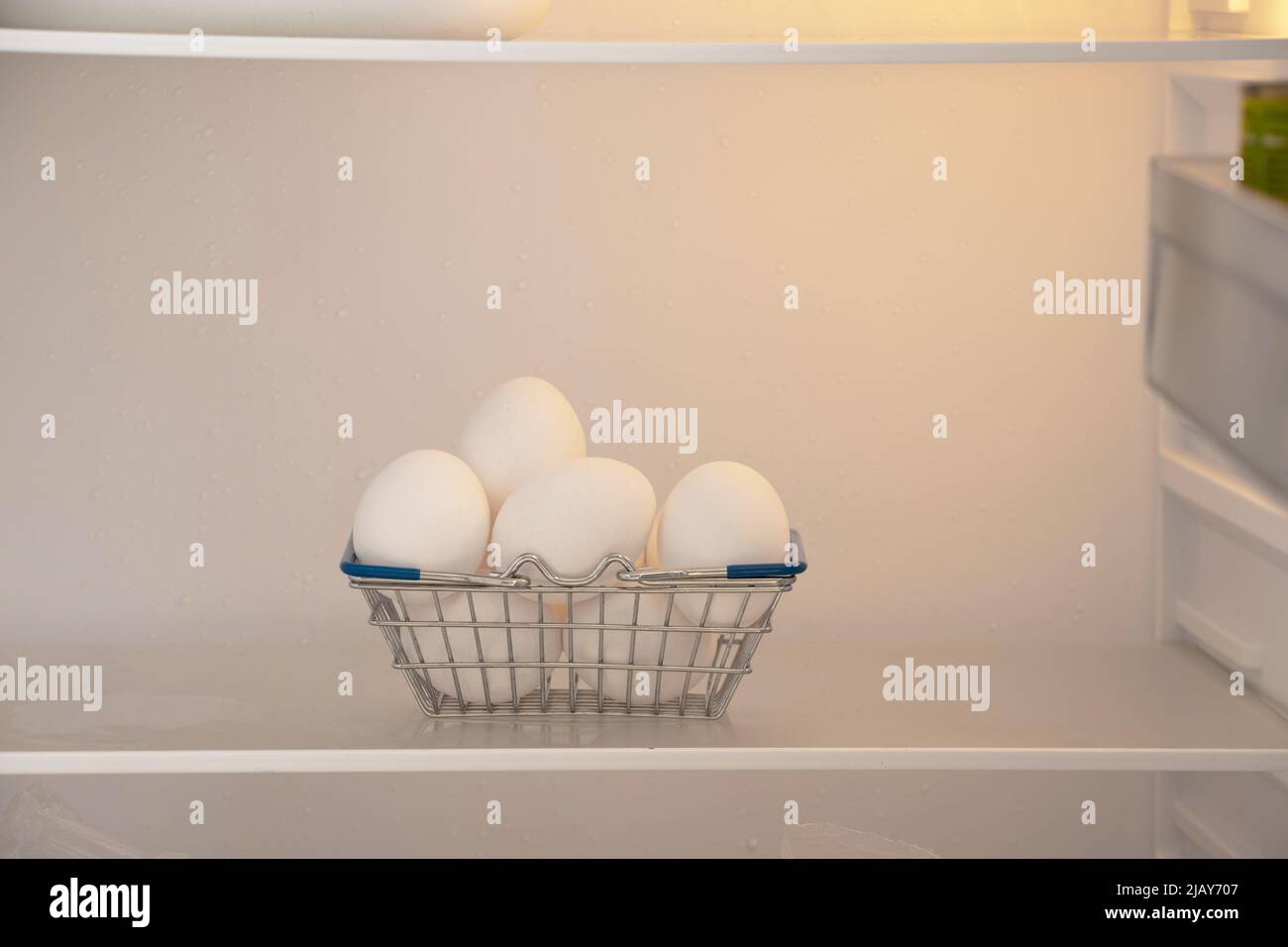 A basket from a supermarket with chicken white eggs on a shelf in the refrigerator, food in the refrigerator on the shelf Stock Photo