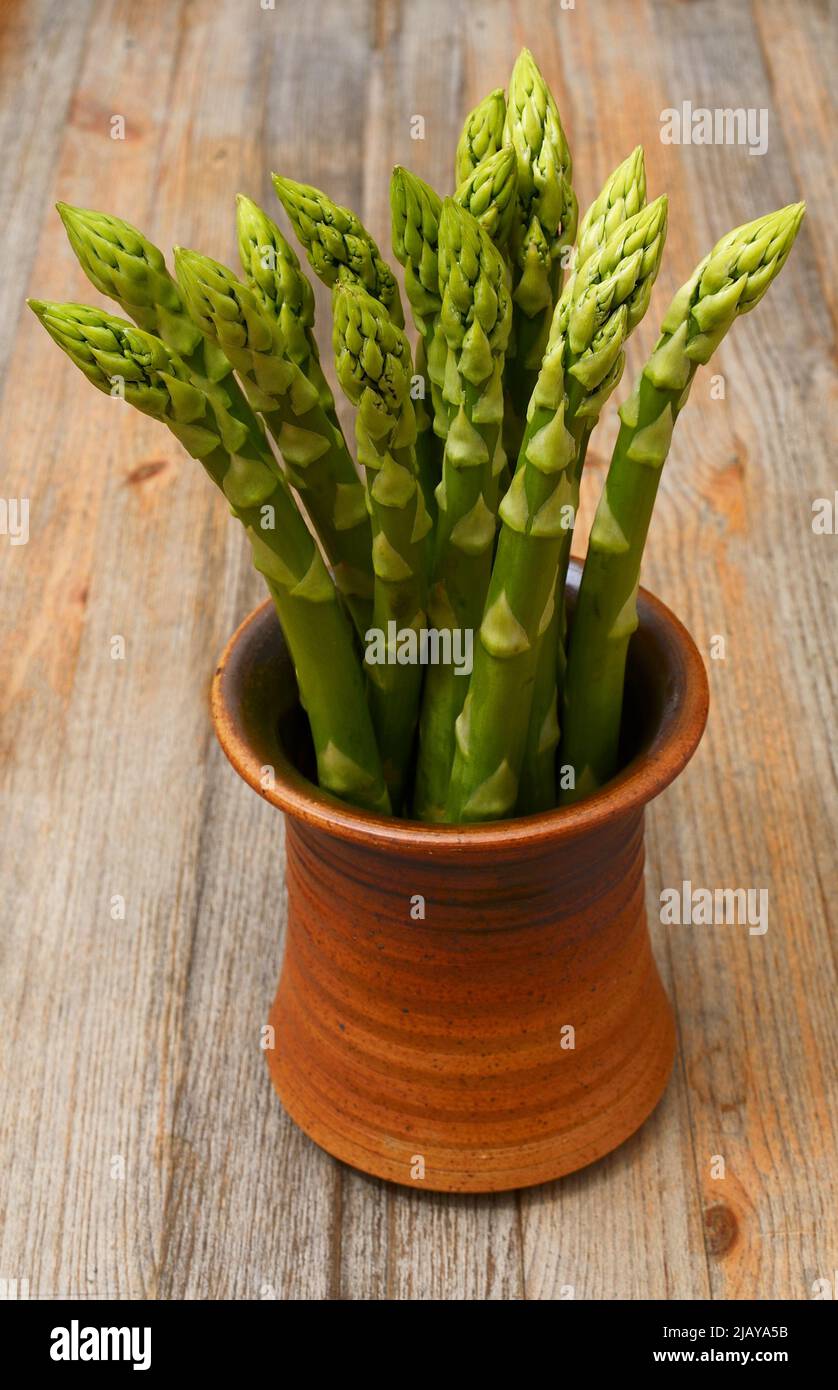a bunch of asparagus in a ceramic pot on a wooden background Stock Photo