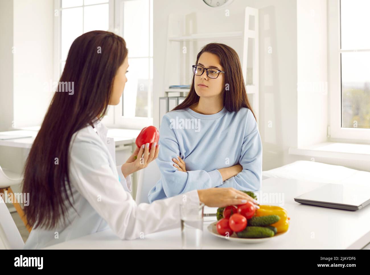 Nutritionist teaches young woman to eat healthy food and talks about benefits of raw vegetables. Stock Photo