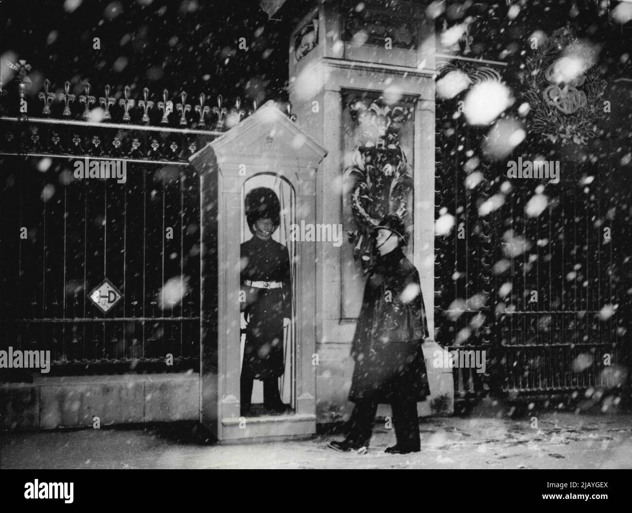 His Regiment Has Just Returned From Malaya - A policeman wales past the sentry in his box outside Buckingham Palace, today Dec 4th, at 3.30 p.m., during London's first heavy fall of snow. The guard is of the 2nd battalion coldstream guards, which has just returned from service in Malaya, and is now carrying out guard duty at the Palace. December 4, 1950. (Photo by Associated Press Photo). Stock Photo