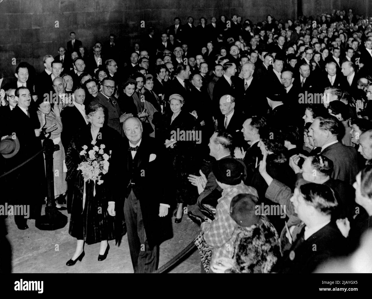 Premier Makes Triumphal Exit From Westminster Hall: Sir Winston and Lady Churchill beam their acknowledgment of the applause as they leave historic Westminster Hall, London, to-day (Tuesday) after the presentations to Sir Winston on his 80th birthday. Following the Prime Minister and his wife are Mr. and Mrs. Clement Attlee. Mr. Attlee had just presented to Sir Winston the joint gift of both houses of parliament - the premier's portrait in oils by Graham Sutherland. Sir Winston had also received the house of commons gift, a commemorative book signed by nearly all the members. November 30, 1954 Stock Photo