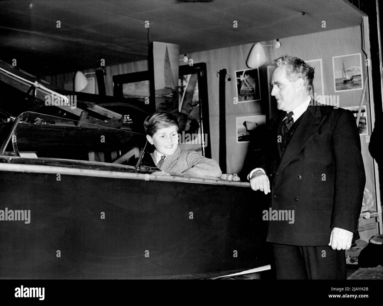 Young Winston Churchill At The Boat Show: Trying out a speedboat at the National Boat show at Olympia is the Prime Ministers grandson, Young Winston Spencer Churchill. There to explain things to him is Mr. Uffa Fox (right) sailing master to H.R.H. The Duke of Edinburgh. Among the thousands of visitors to the National Boat show at Olympia on Saturday, January 1st. was small boy who bears a famous names, Winston Churchill. He is the son of Mr. Randolph Churchill and Grandson of the Prime Minister, after whom he is named, Sir Winston Churchill. January 03, 1955. (Photo by Fox Photos). Stock Photo