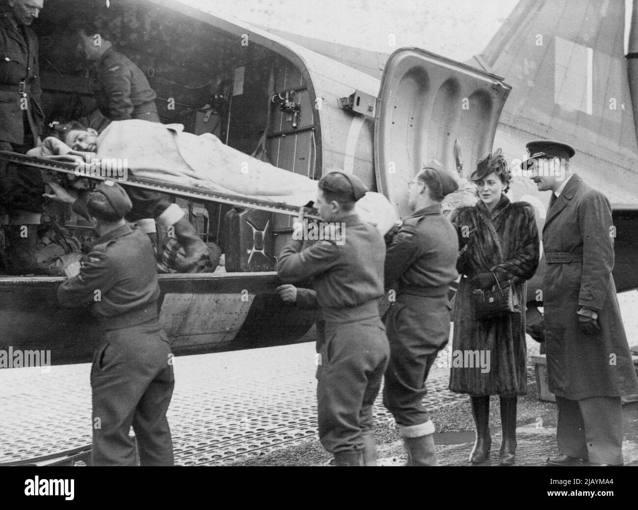 Duchess of Kent Visits West Country Aerodrome -- The Duchess of Kent (right) watches a stretcher case being taken out of a hospital plane. The Duchess of Kent visited a West Country aerodrome where she witnessed the arrival of wounded soldiers, who had been flown over from the Belgian Theatre of War. Since D-Day, R.A.F. Transport Command has flown 50,000 casualties to hospitals in England. December 8, 1944. Stock Photo