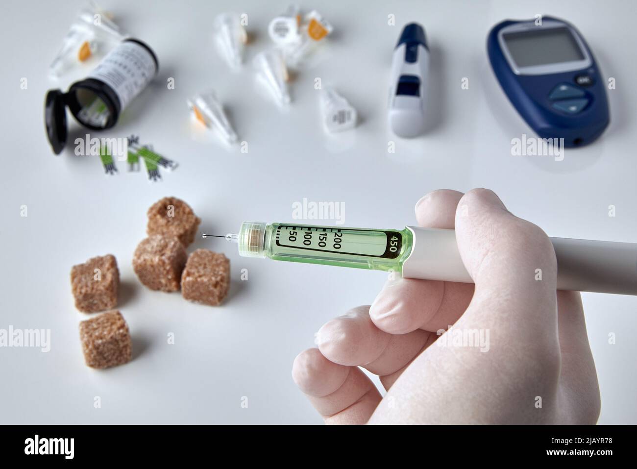 Hands in medical gloves hold a pen with insulin against the background of a glucometer, test strips and sugar. Diabetes treatment concept Stock Photo