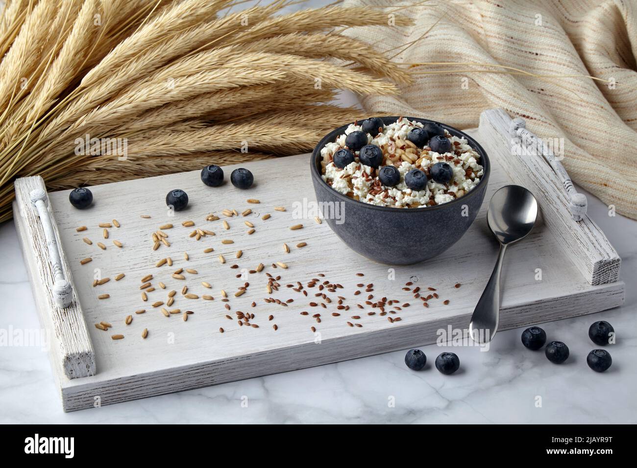 Whole grain oatmeal with blueberries, flax seeds and cottage cheese on a white painted tray surrounded by ears of corn and a tea towel. Energizing bre Stock Photo
