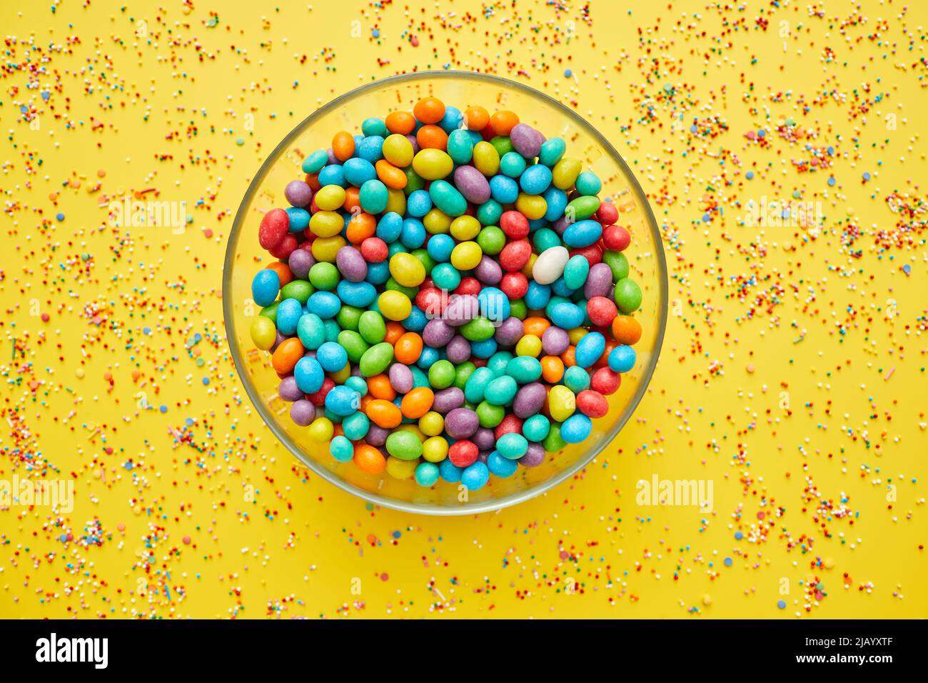 Glassy bowl full of colorful sweet beans on yellow background with splattering sprinkles Stock Photo