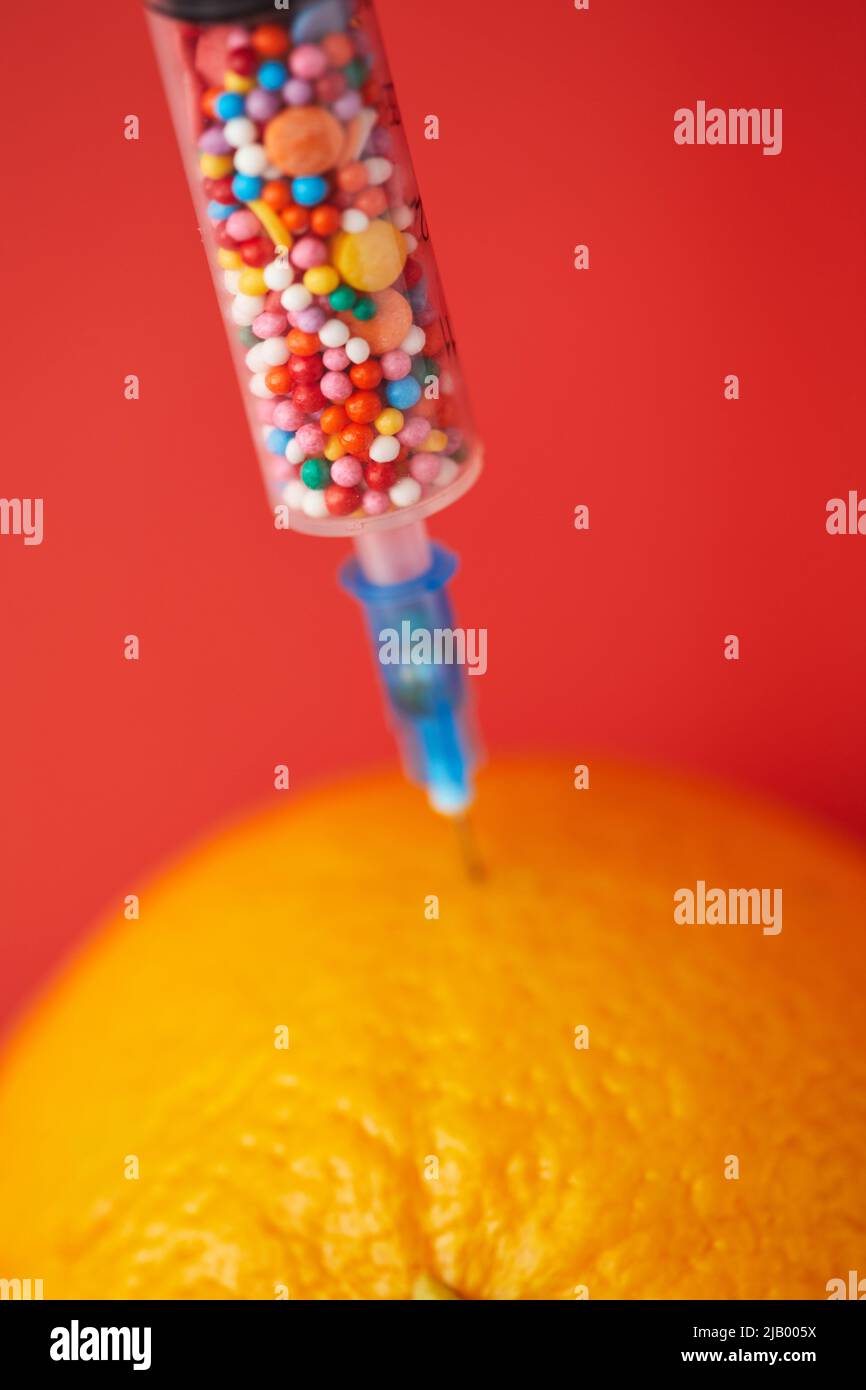Closeup of medical syringe with sweet sprinkles and orange, adding