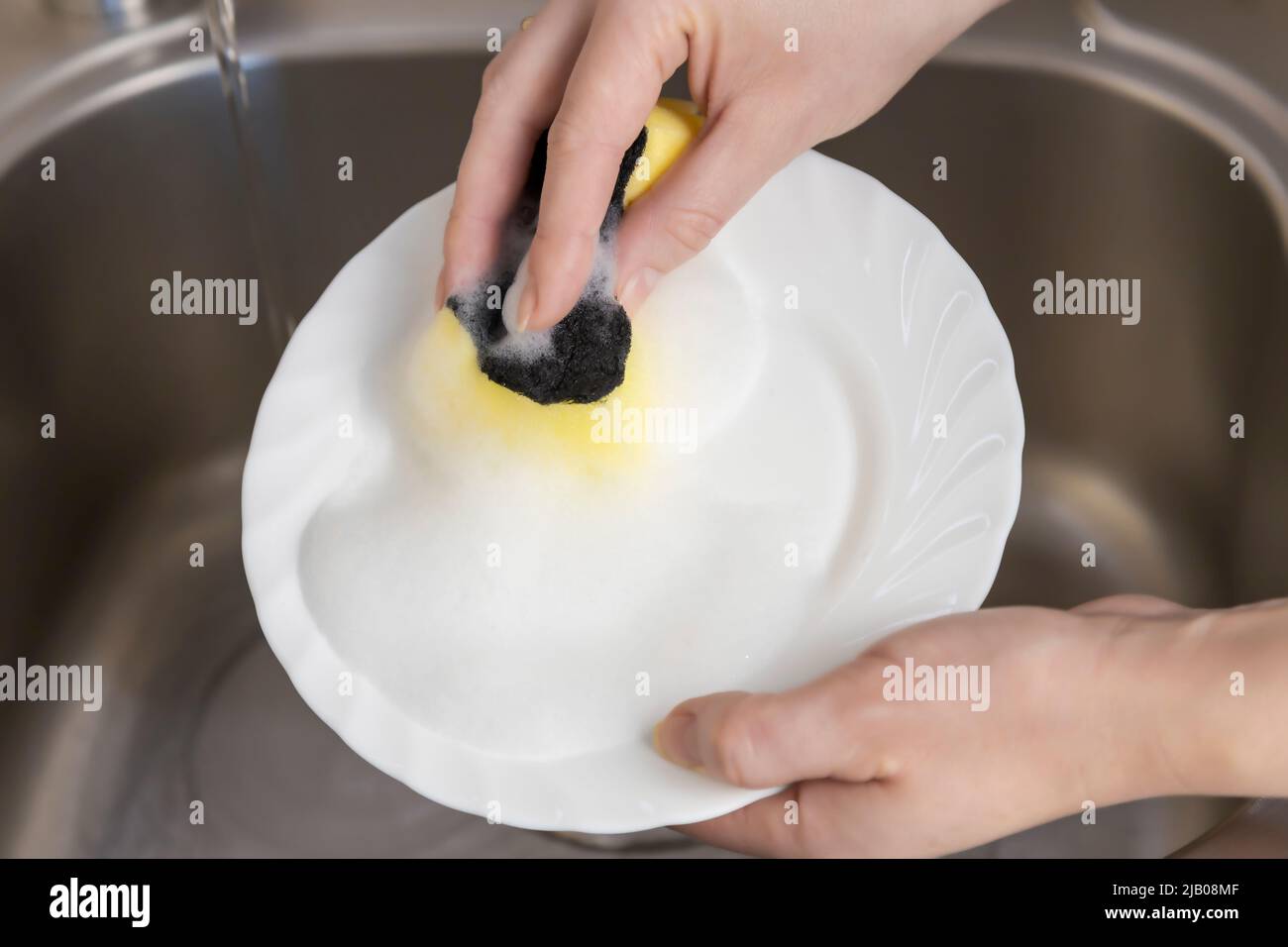 Woman washes a plate in the kitchen under the sink. Top view close up. Stock Photo