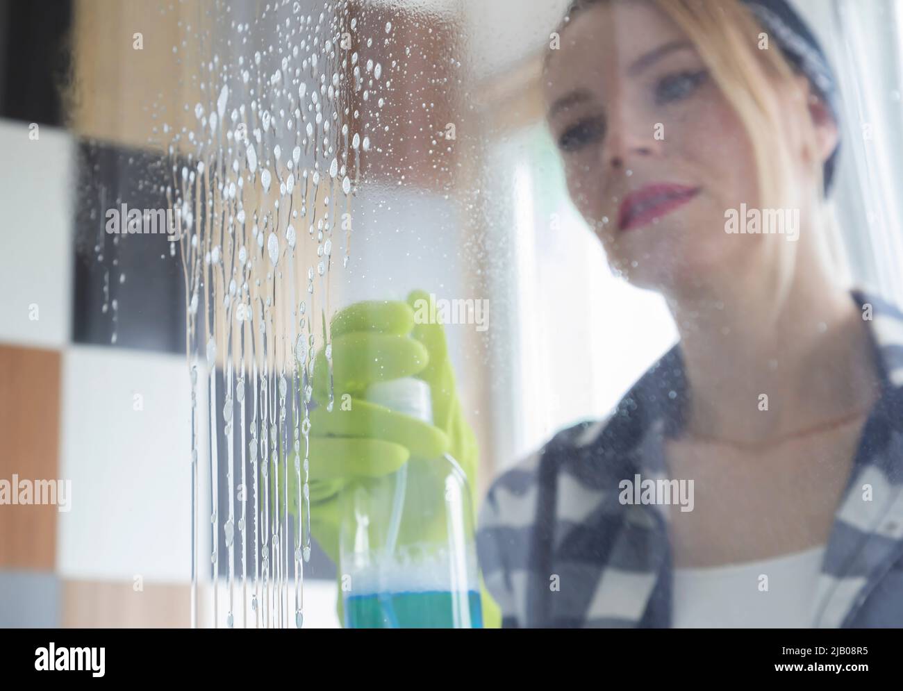 Cleaning the glass from dirt. Woman in green gloves washes the window with a blue cloth. Stock Photo