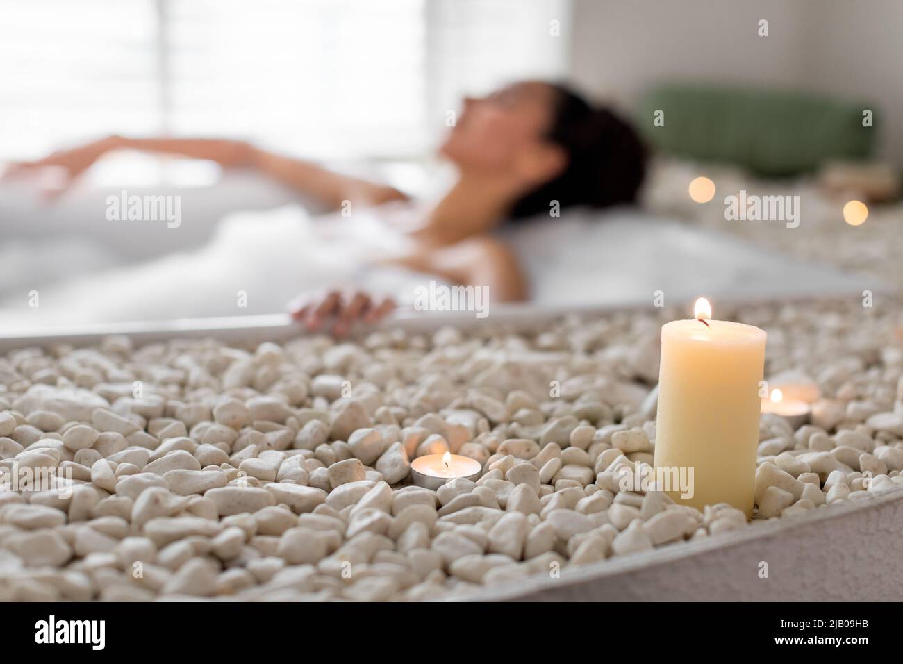Millennial woman relaxing in bathtub with foam, having spa day at home, selective focus on candles and pebbles Stock Photo