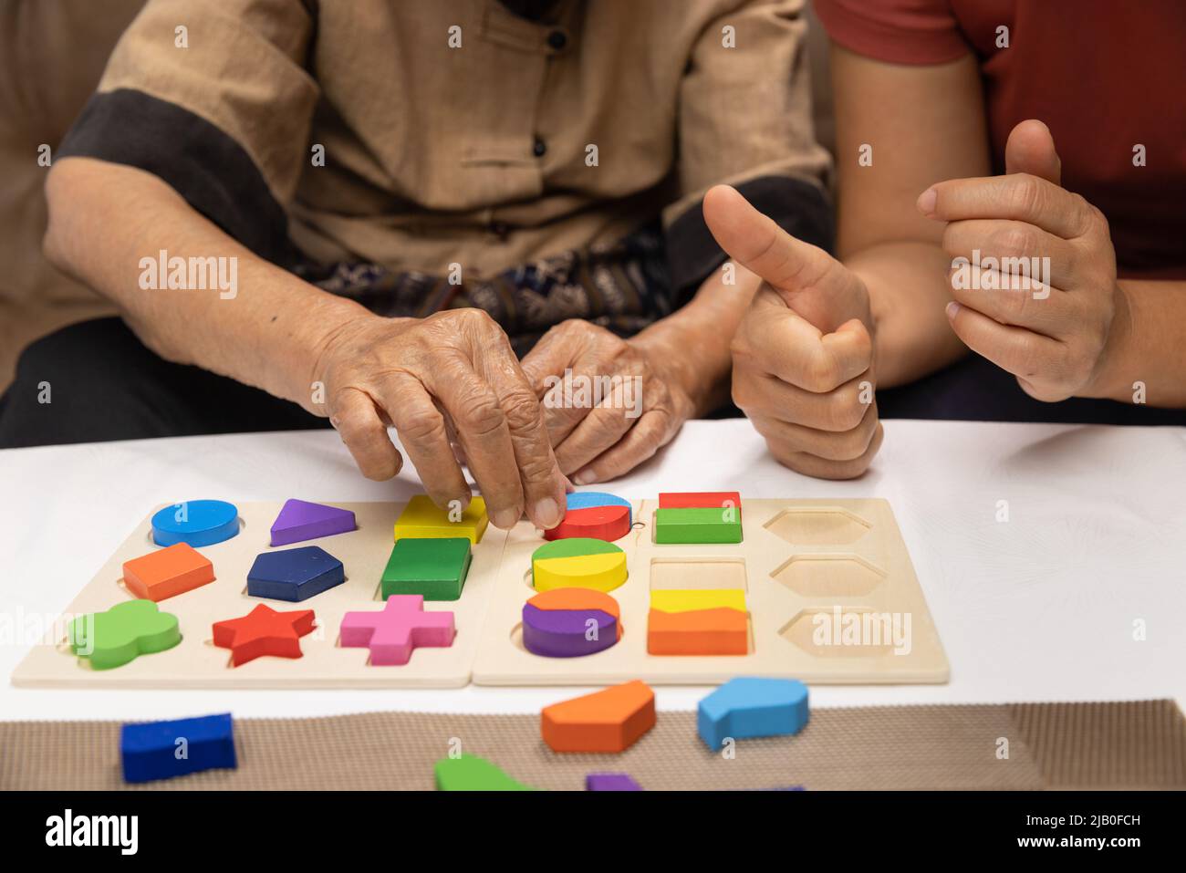 Caregiver and senior woman playing wooden shape puzzles game for