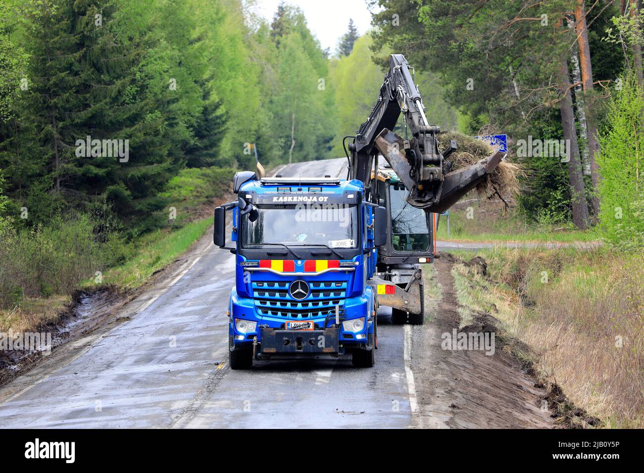 Blue Mercedes-Benz Arocs tipper truck and excavator of Kaskenoja Oy at work clearing ditches at Fiskarsintie. Road 104, Ansku, Finland. May 26, 2022. Stock Photo