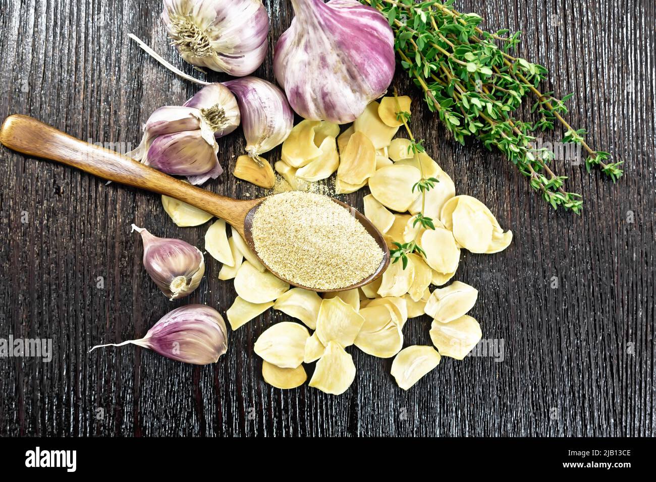 Ground garlic in a spoon, dried and fresh garlic, bunch of thyme on wooden board background from above Stock Photo