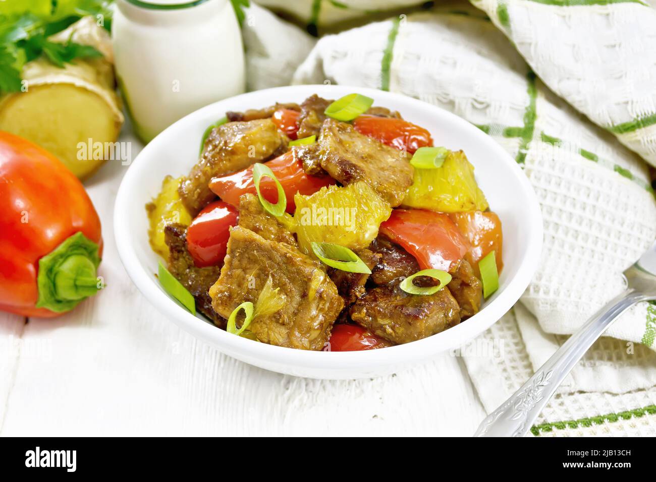 Beef with oranges, bell pepper and ginger root in bowl, a towel and a fork on the background of light wooden board Stock Photo