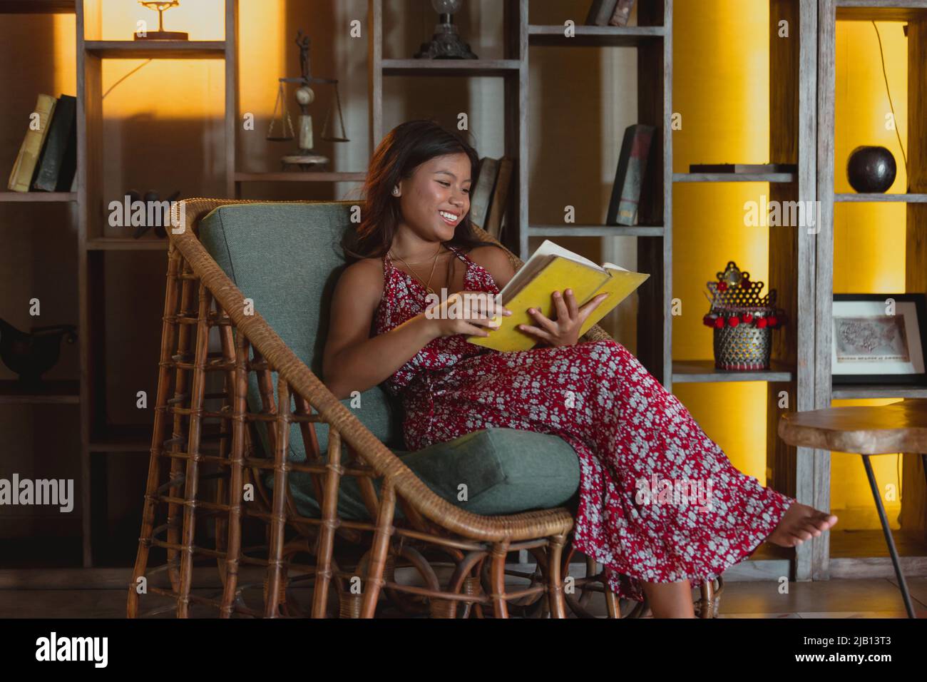 young tan asian female sitting in a hotel lobby reading a yellow book waiting to checkin Stock Photo