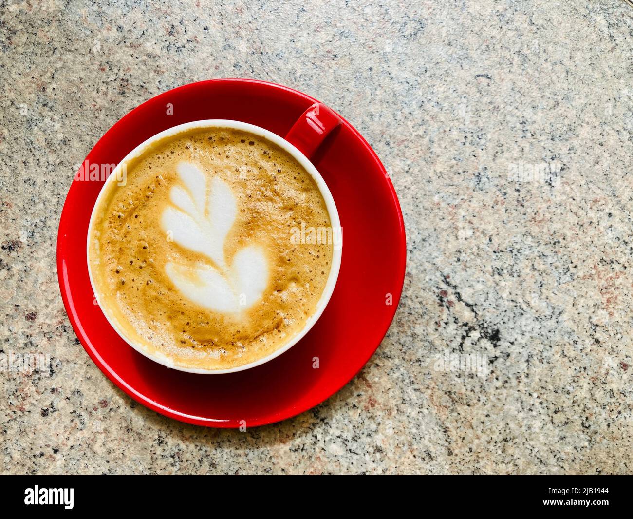A flat white coffee in a red mug and saucer. Decorative coffee art