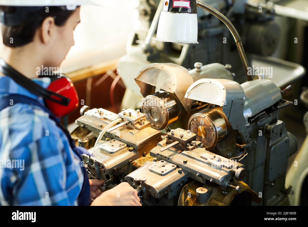 Over shoulder view of busy female engineer adjusting lathe machine for designing details at wristwatch factory Stock Photo