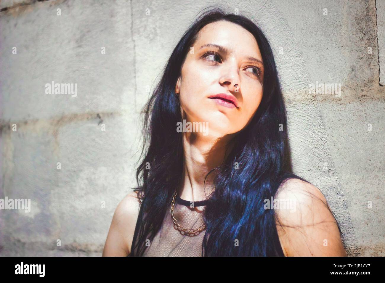 A goth girl leaning against a wall looking away from the camera Stock Photo