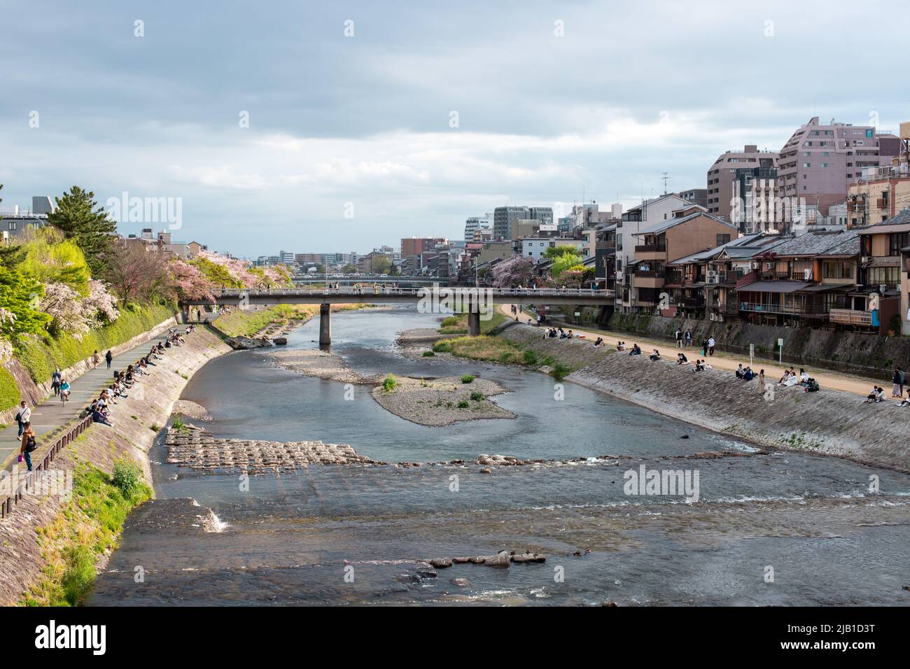 Kamo River (Kamo-gawa), which means 'duck river' in Japanese runs throughout Kyoto prefecture, in cloudy day. Local people sitting by the riverside Stock Photo