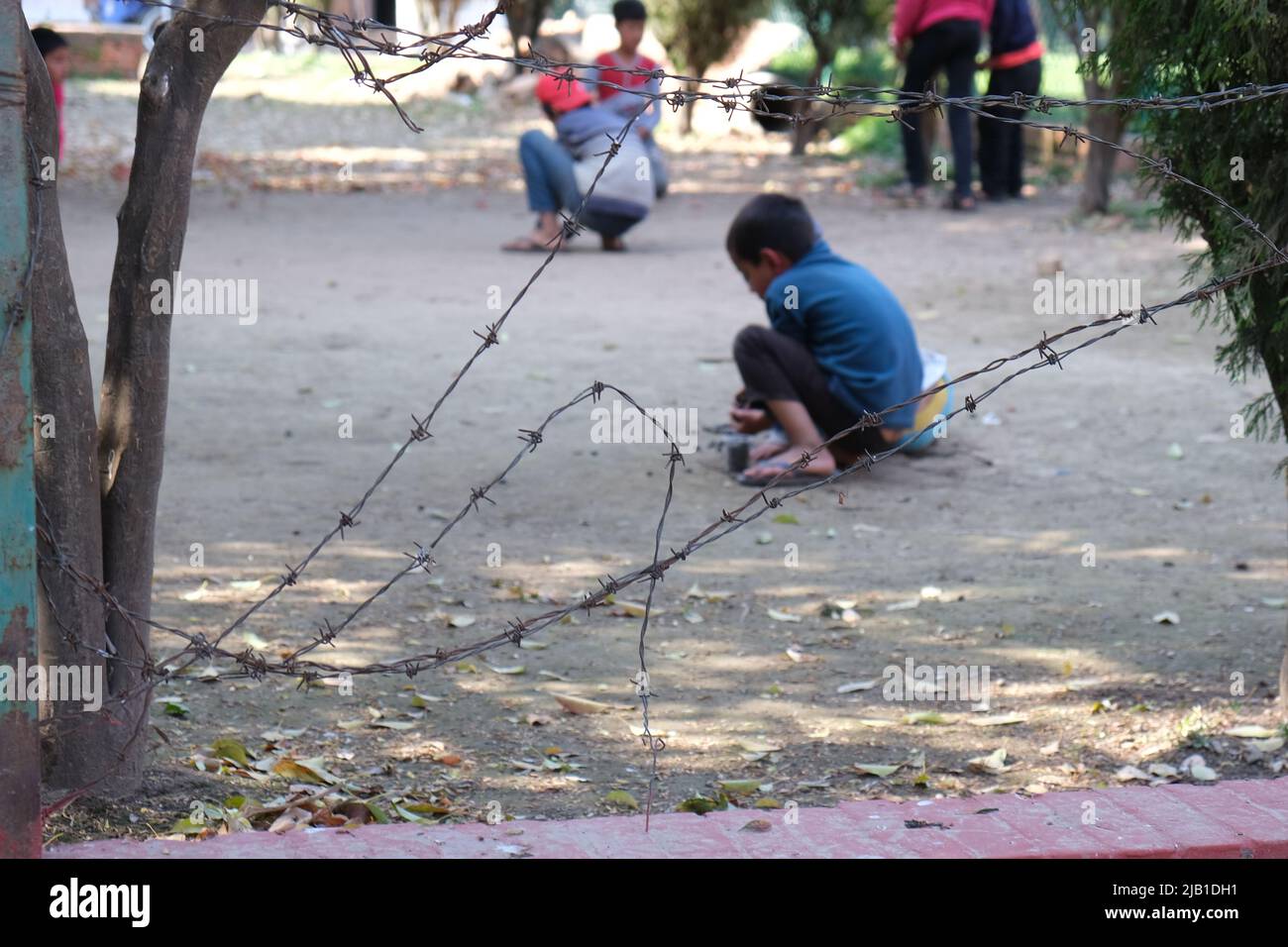 Unrecognized children playing in a playground behind a barbed metal fence Stock Photo