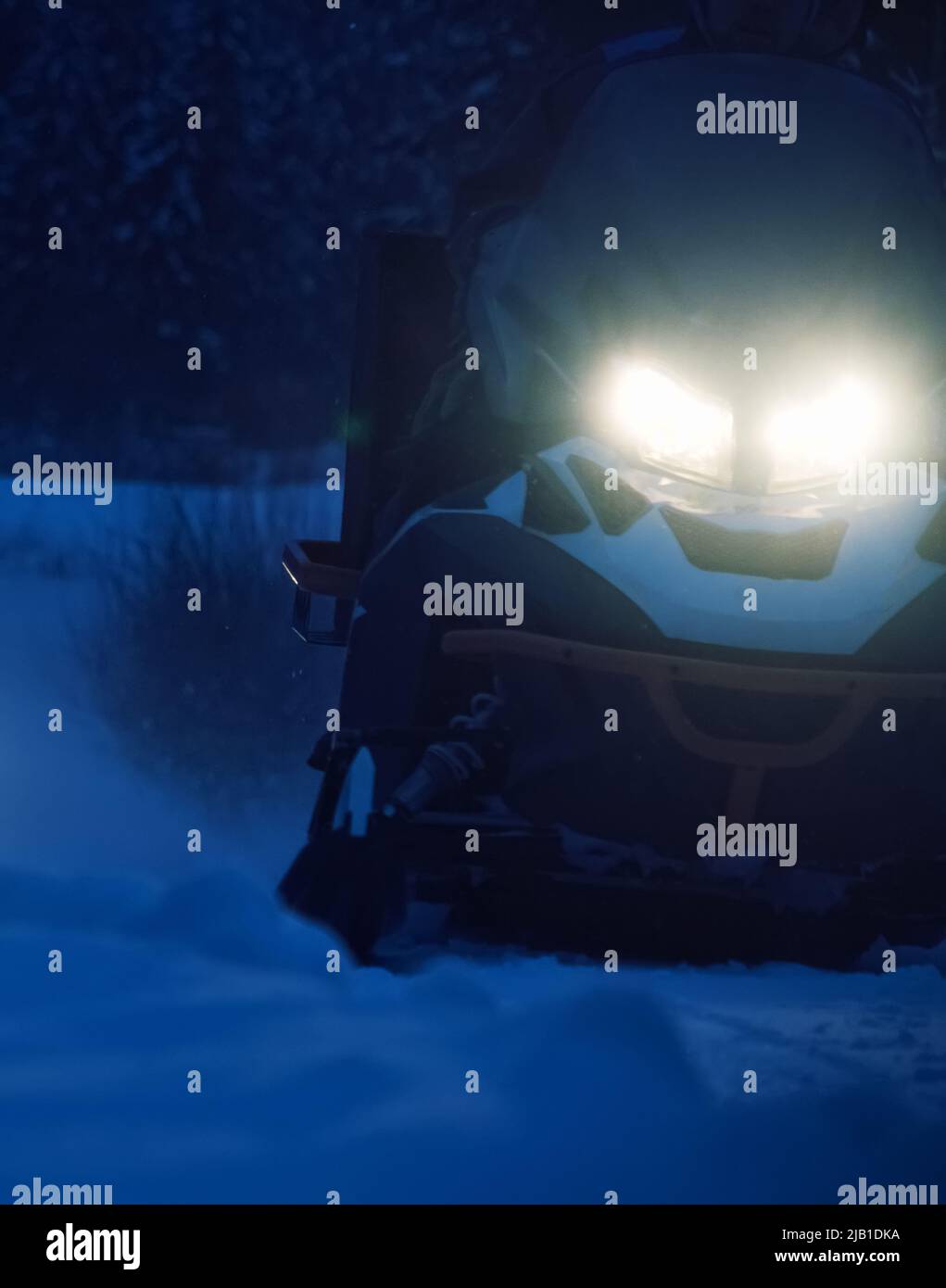 A snowmobile rides on a snowy road at night with its headlights on
