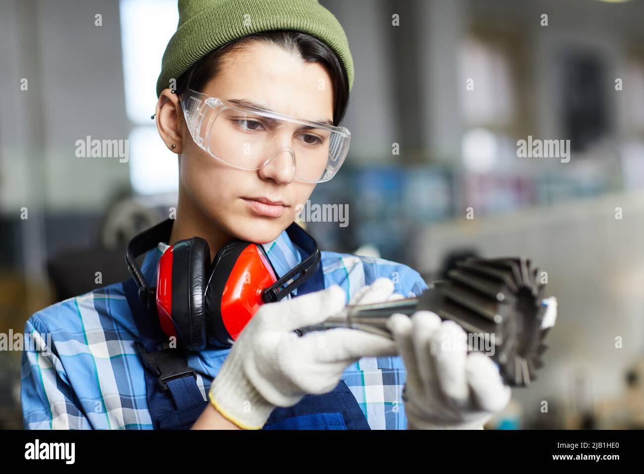 Serious thoughtful attractive female engineer in transparent safety goggles examining milling machine tool while finding out reason of breakage Stock Photo